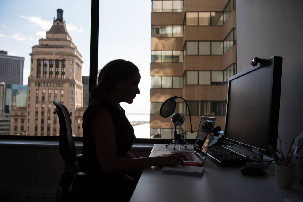 Woman working at computer in front of a large window overlooking buildings